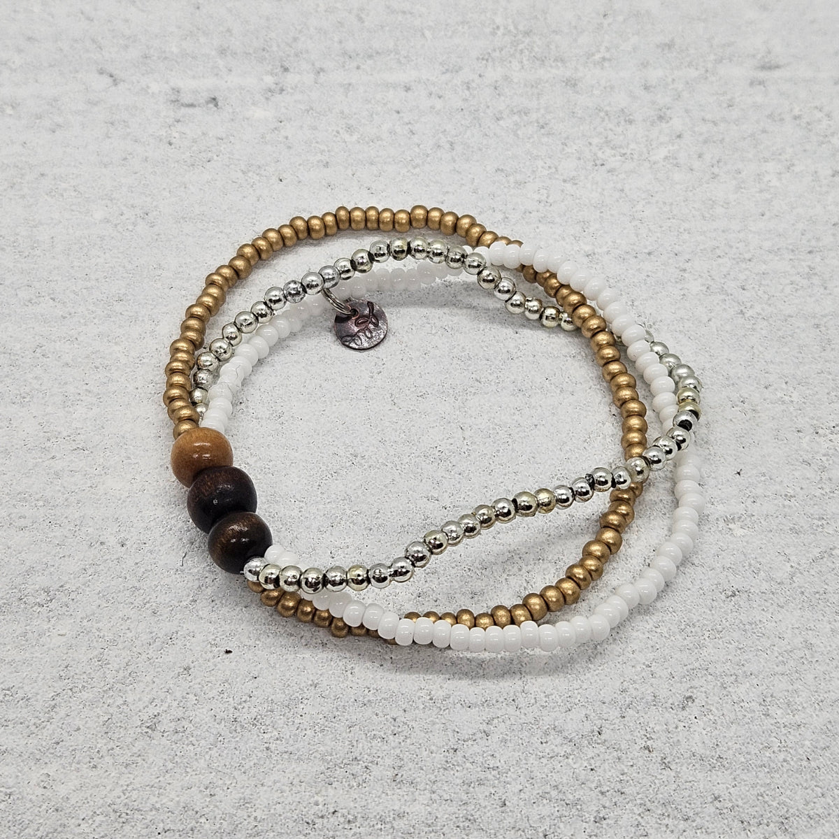 Elastic bracelet made of 3 strands of seed beads, gold, silver, white, connected with 3 wood beads.